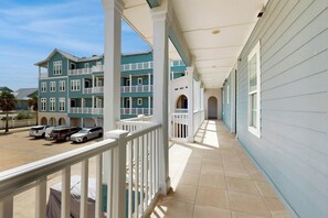 A covered corridor with a view of a multi-story building with balconies and parked vehicles. - Gulf Views | Chef’s Kitchen | Beach Escape (Port Aransas)
