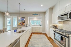 Een moderne keuken met witte kasten, een centraal eiland, een groot raam en een roestvrijstalen afzuigkap.