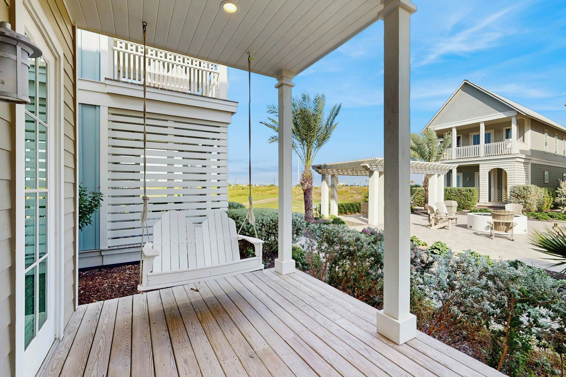 A wooden deck with a covered area, a white railing, and a view of a house with a covered patio and outdoor furniture.