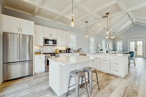 A spacious kitchen with a large island, stainless steel appliances, and a high ceiling with exposed beams. - Paradise Found | Steps to Beach | Resort Amenities (Port Aransas)