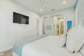 Ein Schlafzimmer mit einem Bett, einem an der Wand montierten Fernseher und einer Tür zu einem anderen Raum.