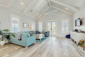 A spacious living room with a high ceiling, a ceiling fan, and a large window with blinds. - Paradise Found | Steps to Beach | Resort Amenities (Port Aransas)