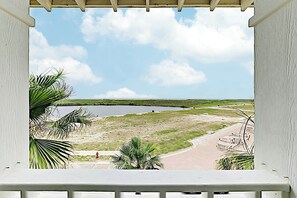A view from a balcony with a clear sky, a body of water, and a road leading to a distant shoreline. - Pearl Over The Pool | Gulf Views | Steps to Beach (Port Aransas)