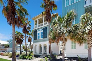 A two-story building with a balcony, surrounded by palm trees and a clear sky. - Pearl Over The Pool | Gulf Views | Steps to Beach (Port Aransas)