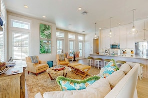 A spacious living room with a sofa, chairs, and a coffee table. There is a kitchen area with a refrigerator, microwave, and bar stools. - Pearl Over The Pool | Gulf Views | Steps to Beach (Port Aransas)