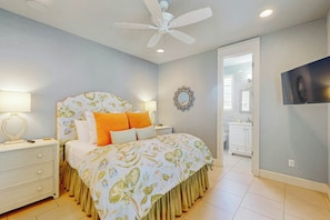A bedroom with a bed, nightstands, a ceiling fan, a mirror, and a bathroom visible through an open door. - Pearl Over The Pool | Gulf Views | Steps to Beach (Port Aransas)