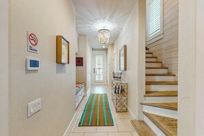 A hallway with a staircase, a chandelier, a 'NO SMOKING' sign, and a patterned rug. - Pearl Over The Pool | Gulf Views | Steps to Beach (Port Aransas)