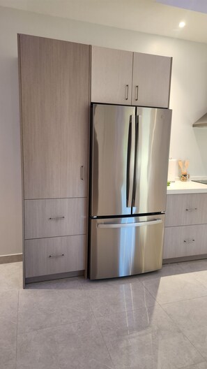 A stainless steel refrigerator with two doors, a wooden cabinet with drawers, and a countertop with a mug and utensils. - Poolside One-Bedroom Retreat @ Villa Troyanda in Grace Bay (Providenciales)