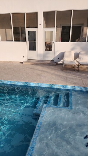 A swimming pool with a tiled edge, a covered patio area with chairs, and a building with large windows. - Poolside One-Bedroom Retreat @ Villa Troyanda in Grace Bay (Providenciales)