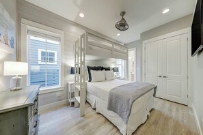 Ein Schlafzimmer mit Etagenbett, Nachttisch mit Lampe, Fenster mit Jalousien, Deckenventilator und einer Tür.