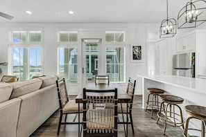 A modern kitchen with white cabinetry, a stainless steel refrigerator, and a dining area with a wooden table and chairs. - Sabal Good, Man | Beach Getaway | Resort Amenities (Port Aransas)