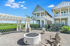 Ein zweistöckiges Haus mit überdachter Terrasse, Sitzgelegenheiten im Freien und einem angelegten Garten.