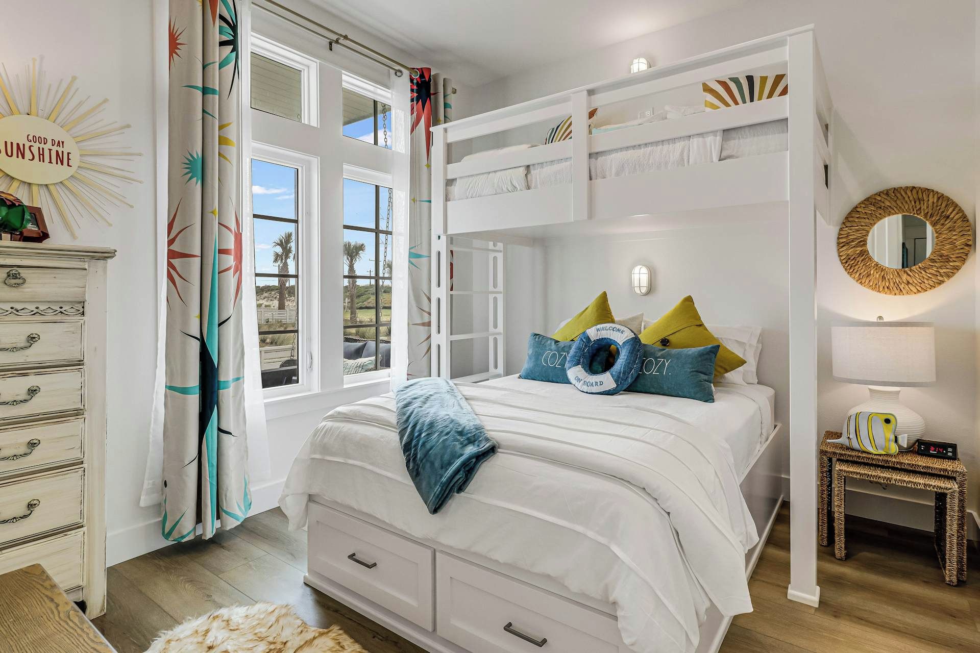 Une chambre avec un lit superposé, une commode, une table de chevet avec une lampe, et une vue sur l’extérieur par une fenêtre.