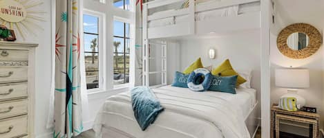 Een slaapkamer met een stapelbed, een dressoir, een nachtkastje met een lamp en uitzicht op het landschap door een raam.
