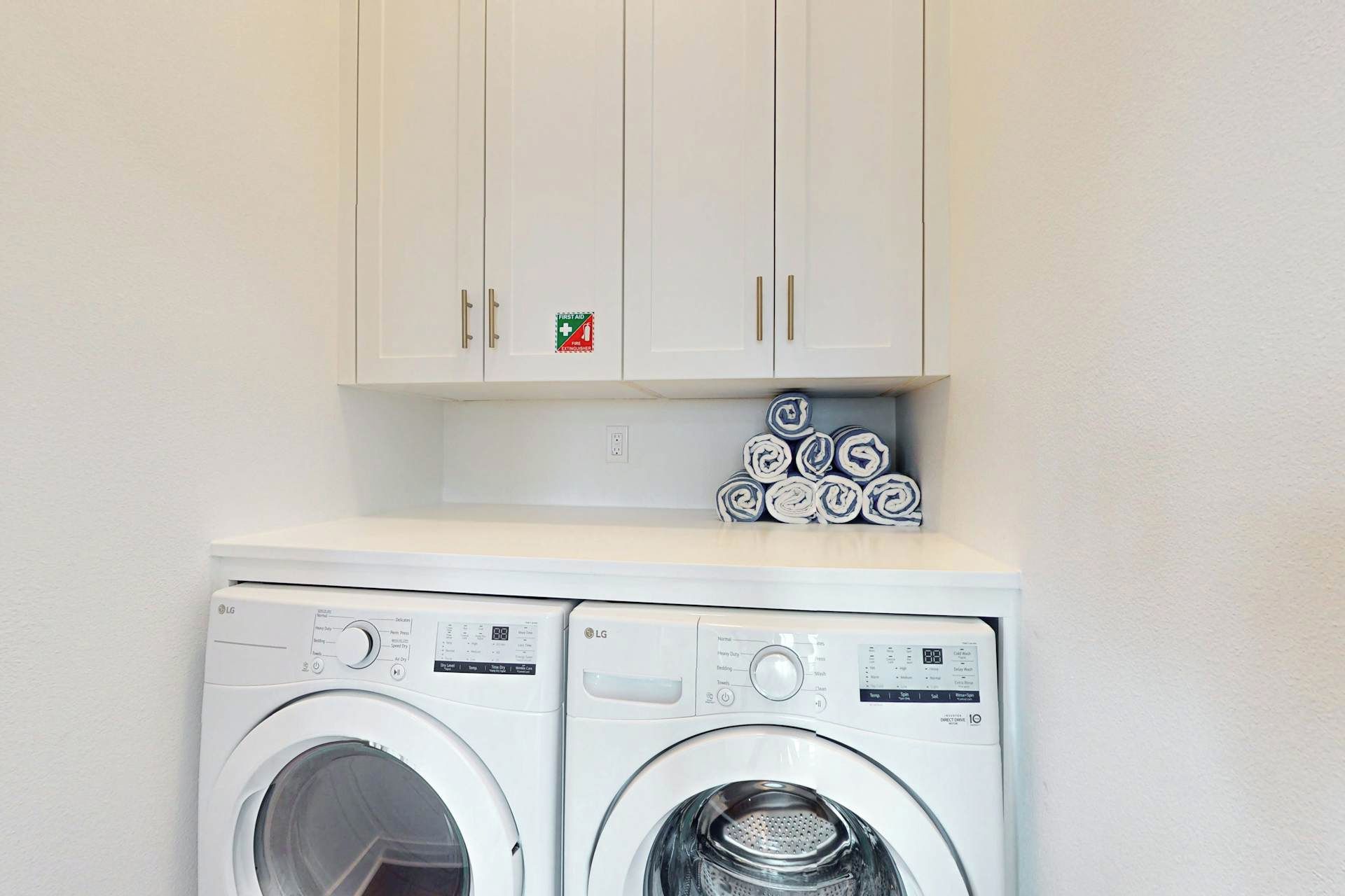 A laundry area with two white washing machines, a cabinet above, and a stack of rolled towels.