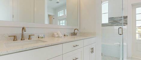 A modern bathroom with a large mirror, a shower with a glass door, and a marble-tiled floor.