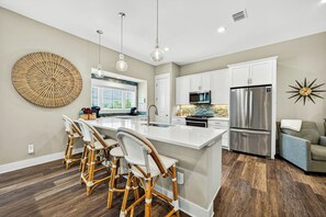 A modern kitchen with a central island, white cabinetry, and a stainless steel refrigerator. - Sea Gem | Golf Views | Steps to Beach (Port Aransas)