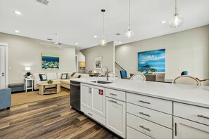 A modern kitchen with a central island, white cabinetry, and pendant lighting. - Sea Gem | Golf Views | Steps to Beach (Port Aransas)