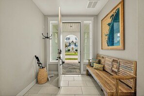 A hallway with a bench, a door leading to a house, and a framed map on the wall. - Sea Gem | Golf Views | Steps to Beach (Port Aransas)