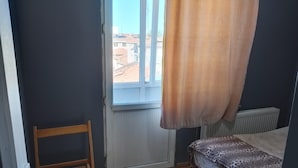 Una habitación pequeña con una cama individual, una silla, un radiador y una ventana con cortina.