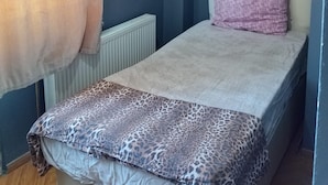 Una habitación pequeña con una cama individual, cabecera sencilla, un radiador y un enchufe en la pared.