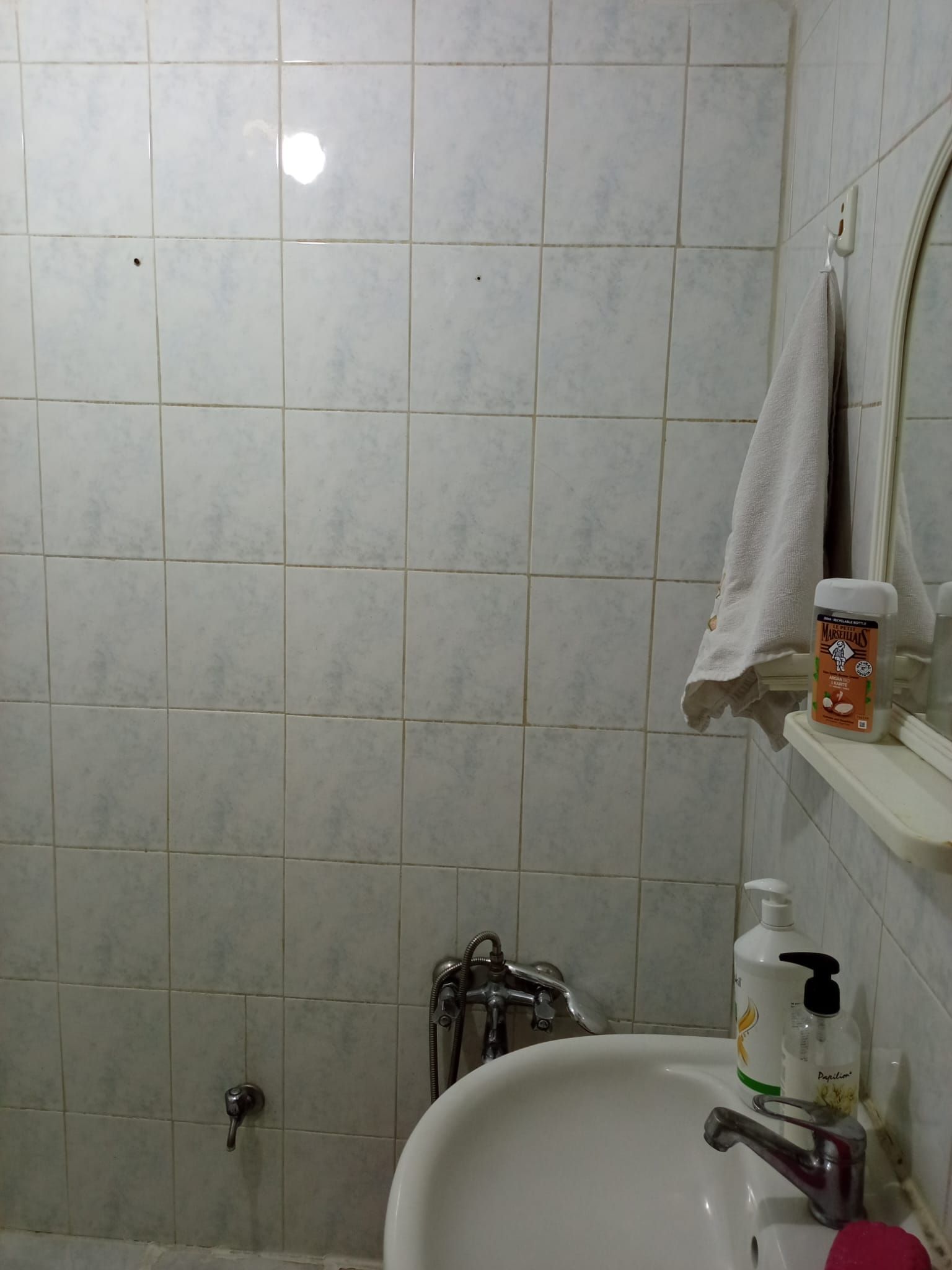Un baño con un lavamanos blanco, un espejo, una toalla colgada en la pared y una botella de jabón.