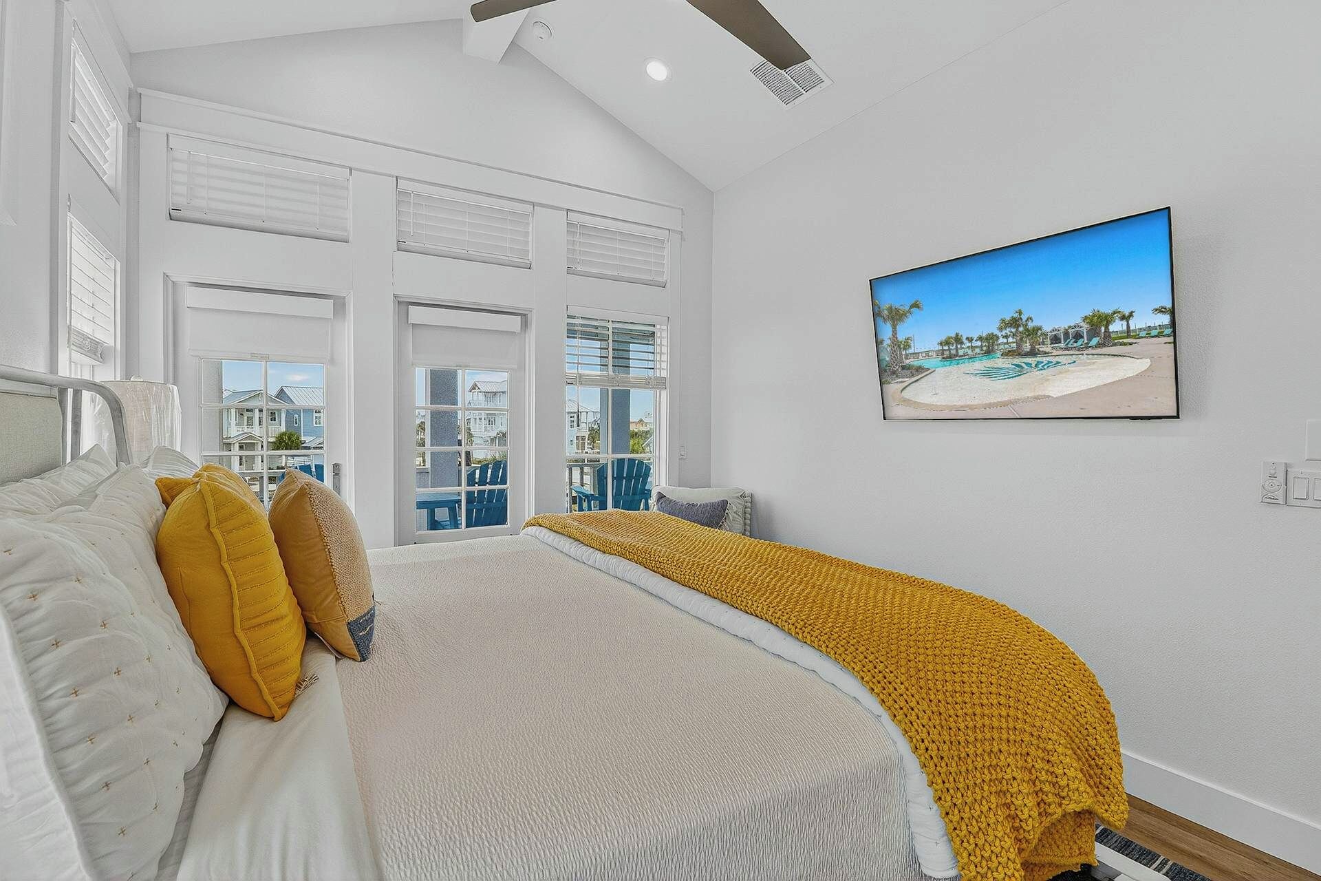 Une chambre à coucher avec un lit, une fenêtre avec des stores, un tableau représentant une plage et une vue sur l’extérieur.