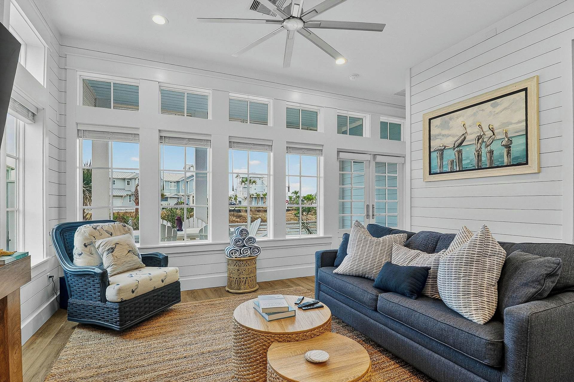 A spacious living room with a large window, a ceiling fan, a blue sofa, and a wicker chair.