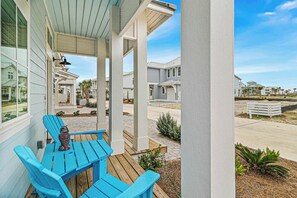 Uma área de estar coberta ao ar livre, com mesa e cadeiras, varanda com colunas e vista para casas vizinhas.