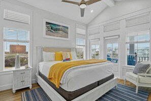 Quarto com cama, mesa de cabeceira, luminária, pintura e vista para o exterior.