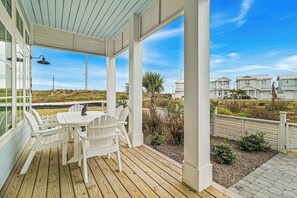 A covered outdoor seating area with a table and chairs, overlooking a residential area with houses and a clear sky. - Siren Song | Steps to Beach | Resort Amenities (Port Aransas)