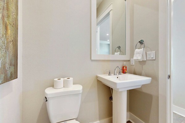 A bathroom with a white toilet, a sink, and a mirror. - Sleek Beach | Steps to Beach | Resort Amenities (Port Aransas)
