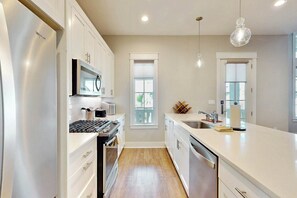 A modern kitchen with white cabinetry, stainless steel appliances, and a central island with a sink. - Sleek Beach | Steps to Beach | Resort Amenities (Port Aransas)