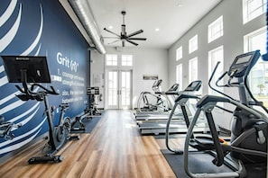 Une salle de sport moderne équipée de machines de cardio, dotée d’un plancher en bois et d’un grand mur bleu orné de messages motivants.