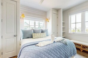 A bedroom with a bed, pillows, a blanket, a bench, and a window. - Sun-Drenched On Sundew | Steps to Beach | Resort (Port Aransas)