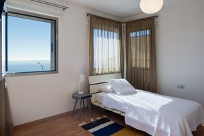 A bedroom with a bed, a bedside table with a lamp, a window with curtains, and a view of the sea. - Villa Sunset Haven Adeje (Adeje)