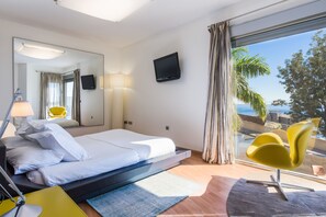 A hotel room with a bed, a TV, a desk, a chair, and a view of the sea. - Villa Sunset Haven Adeje (Adeje)