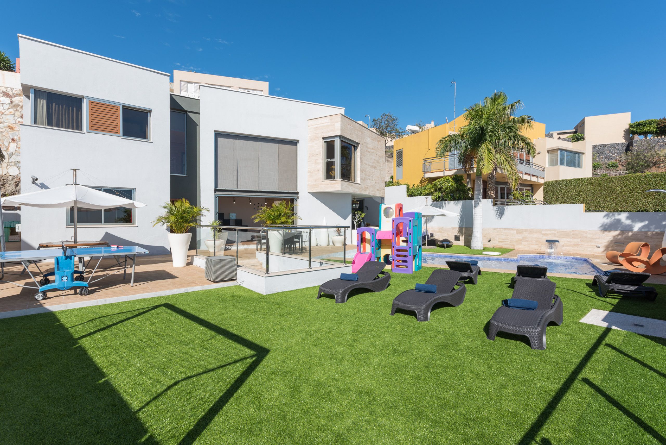 Un espacio exterior moderno con piscina, sillas de descanso y una zona de juegos para niños.