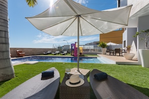 A poolside area with lounge chairs, a sun umbrella, and a small table with a hat and glass. - Villa Sunset Haven Adeje (Adeje)