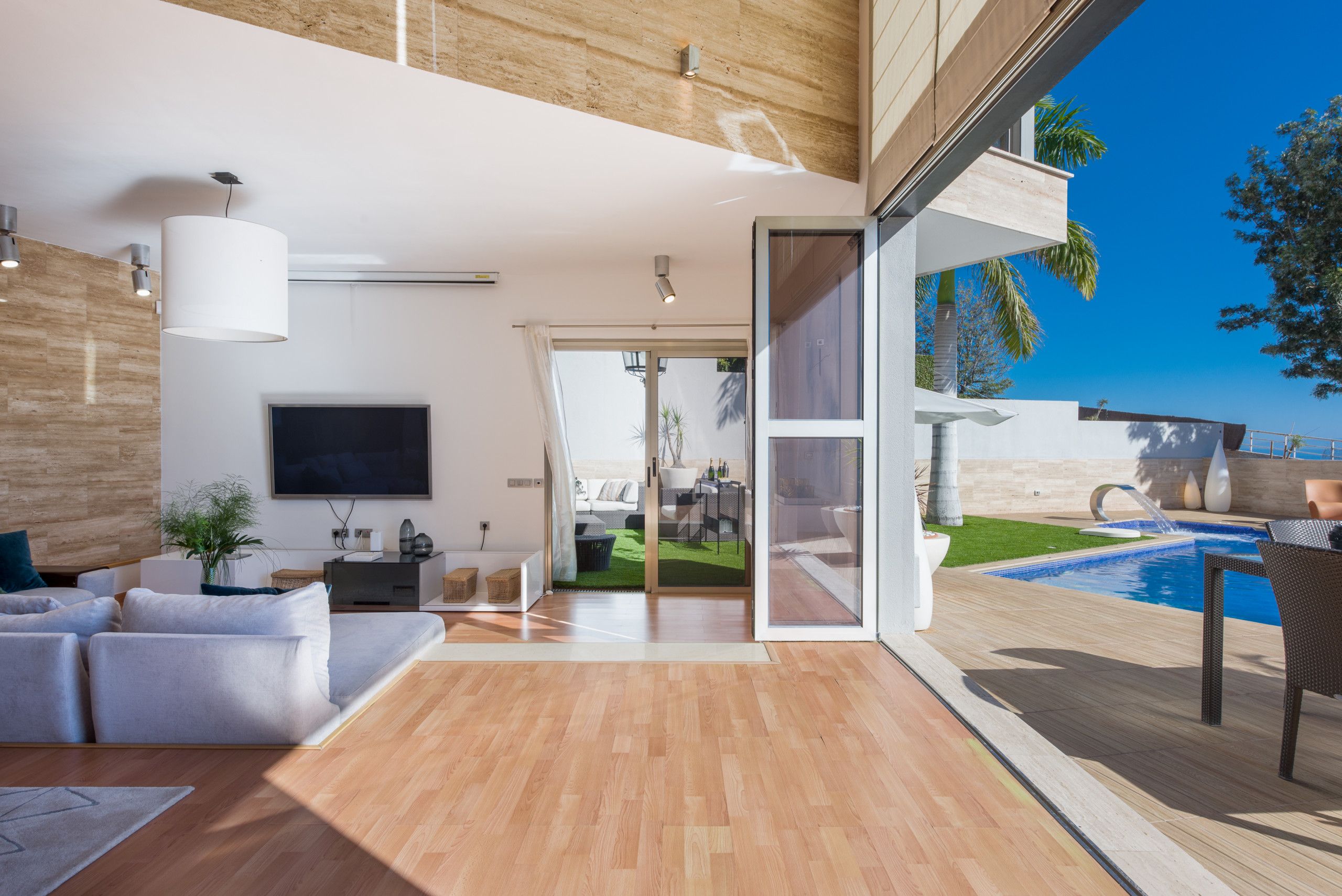 Un salon moderne avec un téléviseur à écran plat, un canapé et une table basse. Une porte vitrée donne accès à un espace extérieur avec une piscine et une vue sur l’océan.