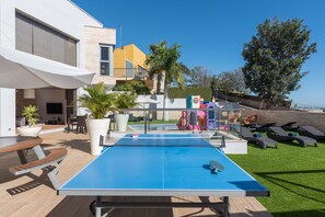 A pool table with a blue surface, surrounded by outdoor seating and a small garden area. - Villa Sunset Haven Adeje (Adeje)