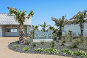 En skylt med ordet ”OASIS” omgiven av en vackert anlagd trädgård med palmer och andra växter.