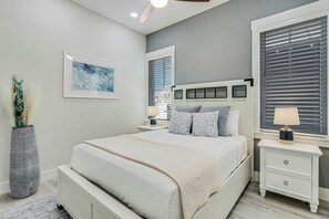 A bedroom with a bed, bedside tables, a nightstand, a lamp, a framed picture, and a window with blinds. - Sunrise Villa | Steps to Beach | Resort Amenities (Port Aransas)