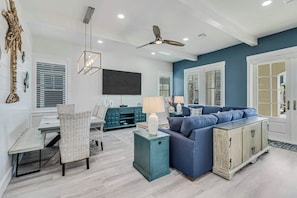 A modern living room with a blue sofa, teal side table, and a ceiling fan. - Sunrise Villa | Steps to Beach | Resort Amenities (Port Aransas)