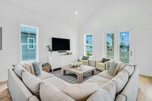 A living room with a sectional sofa, a coffee table, and a flat-screen TV mounted on the wall. - Sunshine Daydream | Golf Views | Steps to Beach (Port Aransas)