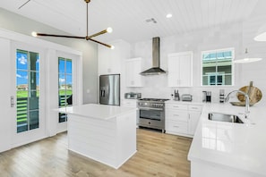 A modern kitchen with white cabinetry, a stainless steel refrigerator, a gas stove, and a large island. - Sunshine Daydream | Golf Views | Steps to Beach (Port Aransas)
