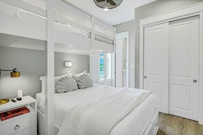 A modern bedroom with a bunk bed, a bedside table with a lamp, and a view of the outdoors through a window. - Sunshine Daydream | Golf Views | Steps to Beach (Port Aransas)