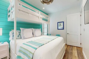 A bunk bed with a striped bedspread, a white nightstand, a white door, and a wall-mounted picture frame. - The Agave Cottage | Beach Escape |Resort Amenities (Port Aransas)
