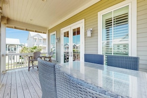 A covered outdoor area with a glass-top table, wicker furniture, and a view of neighboring buildings. - The Agave Cottage | Beach Escape |Resort Amenities (Port Aransas)