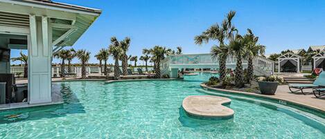 A resort pool area with clear water, palm trees, and a covered seating area.